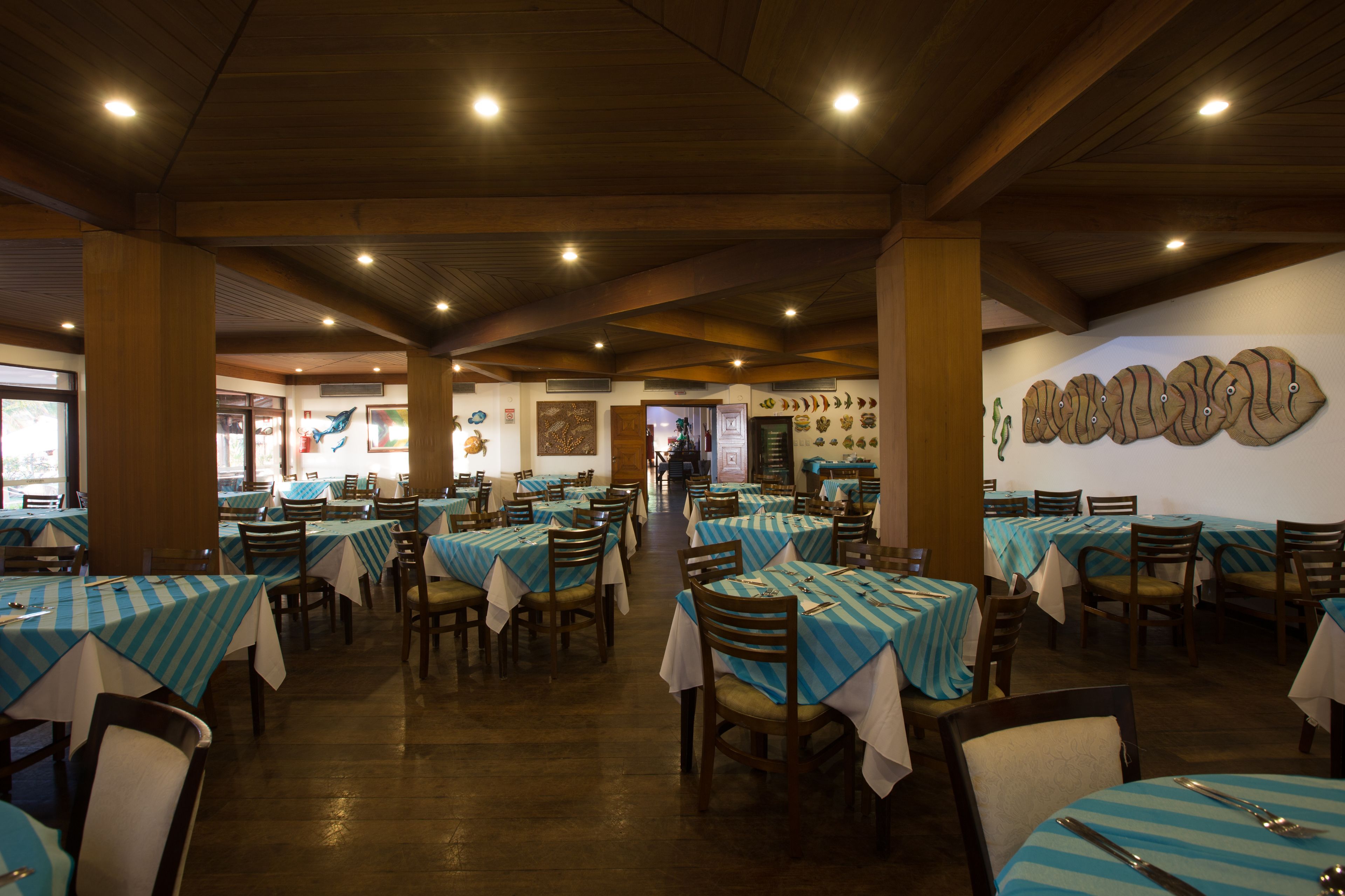 Restaurante com mesas cobertas por toalhas de padrão azul e branco, cadeiras de madeira e teto de madeira com iluminação embutida.