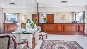 A reception area with a wooden reception desk, glass display cases, and a clock on the wall. - Saint Peter Hotel (São José do Rio Preto)