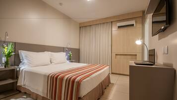 Une chambre d’hôtel avec un grand lit, des tables de chevet, un bureau avec un ordinateur portable, un miroir et un appareil de climatisation.