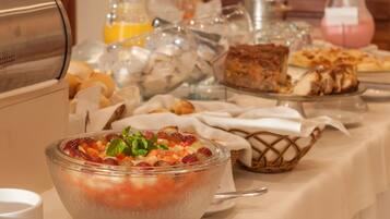 A buffet with various food items including a bowl of fruit salad, bread, and pastries.