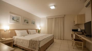 Une chambre d’hôtel comprenant un lit, une table de chevet, une lampe, un bureau, une chaise, une télévision et des rideaux.