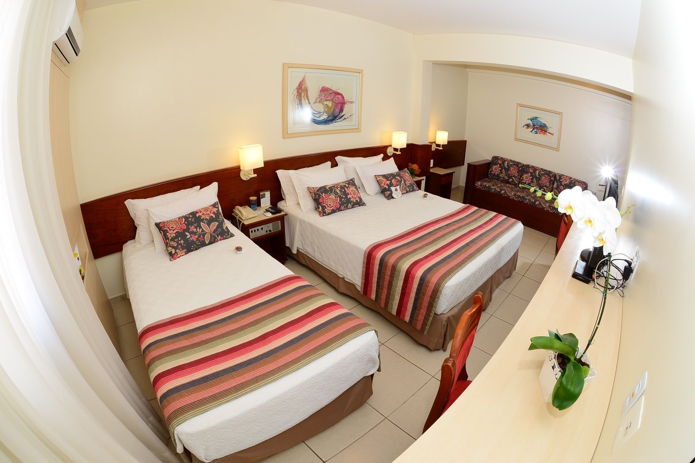 A hotel room with two beds, a sofa, a desk, and a potted plant.