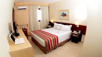 A hotel room with a bed, a desk with a laptop, a telephone, and a nightstand with a lamp.