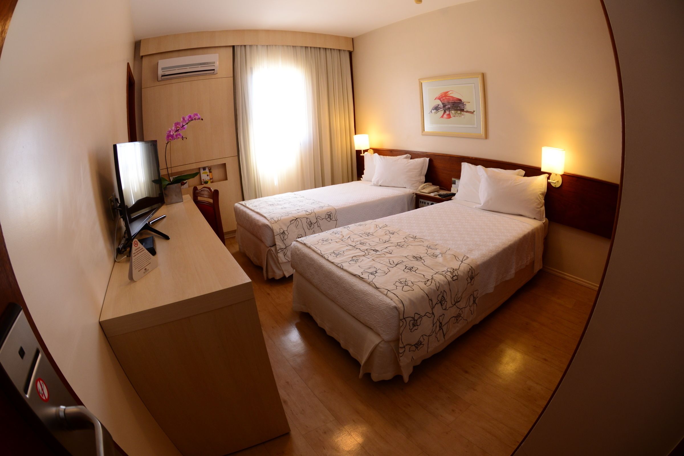 A hotel room with two beds, a desk, a TV, and a window with curtains.