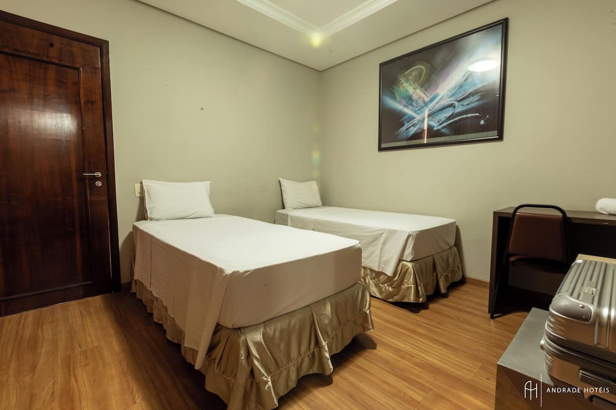 Une chambre d’hôtel avec deux lits, un bureau, une chaise et une valise.