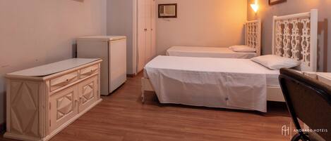 A hotel room with two beds, a wardrobe, a desk, and a television.