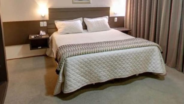 Una habitación de hotel con una cama grande, una mesita de noche, una lámpara de pared y una luz en el techo.