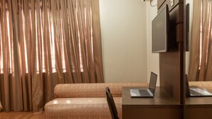 Una habitación con sofá, escritorio con computadora portátil, televisor y ventana con cortinas.
