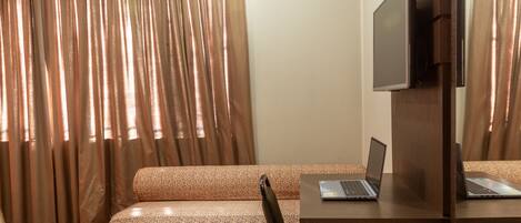 A room with a bed, a desk with a laptop, a television, and a window with curtains.