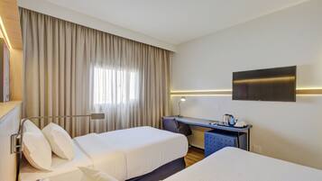 A hotel room with two beds, a desk, a TV, and a window with curtains.