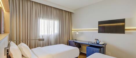 Habitación de hotel con dos camas, un escritorio, un televisor y una ventana con cortinas.