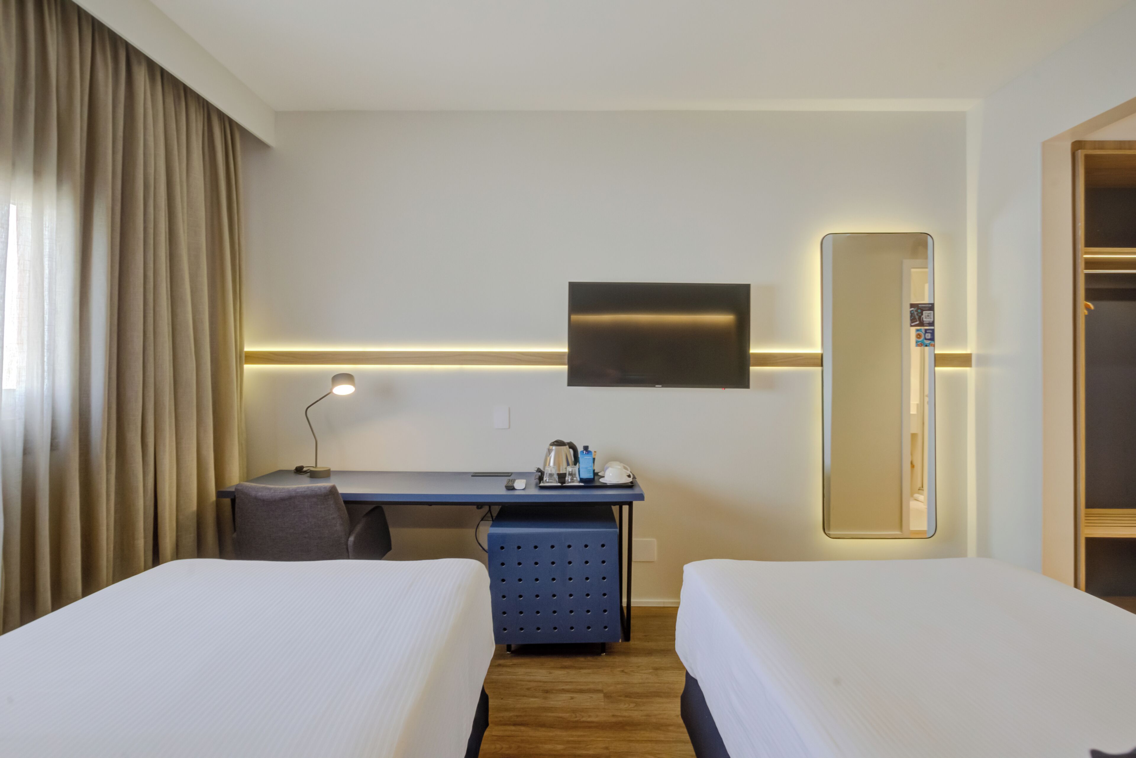 A hotel room with two beds, a desk, a chair, a TV, and a mirror.