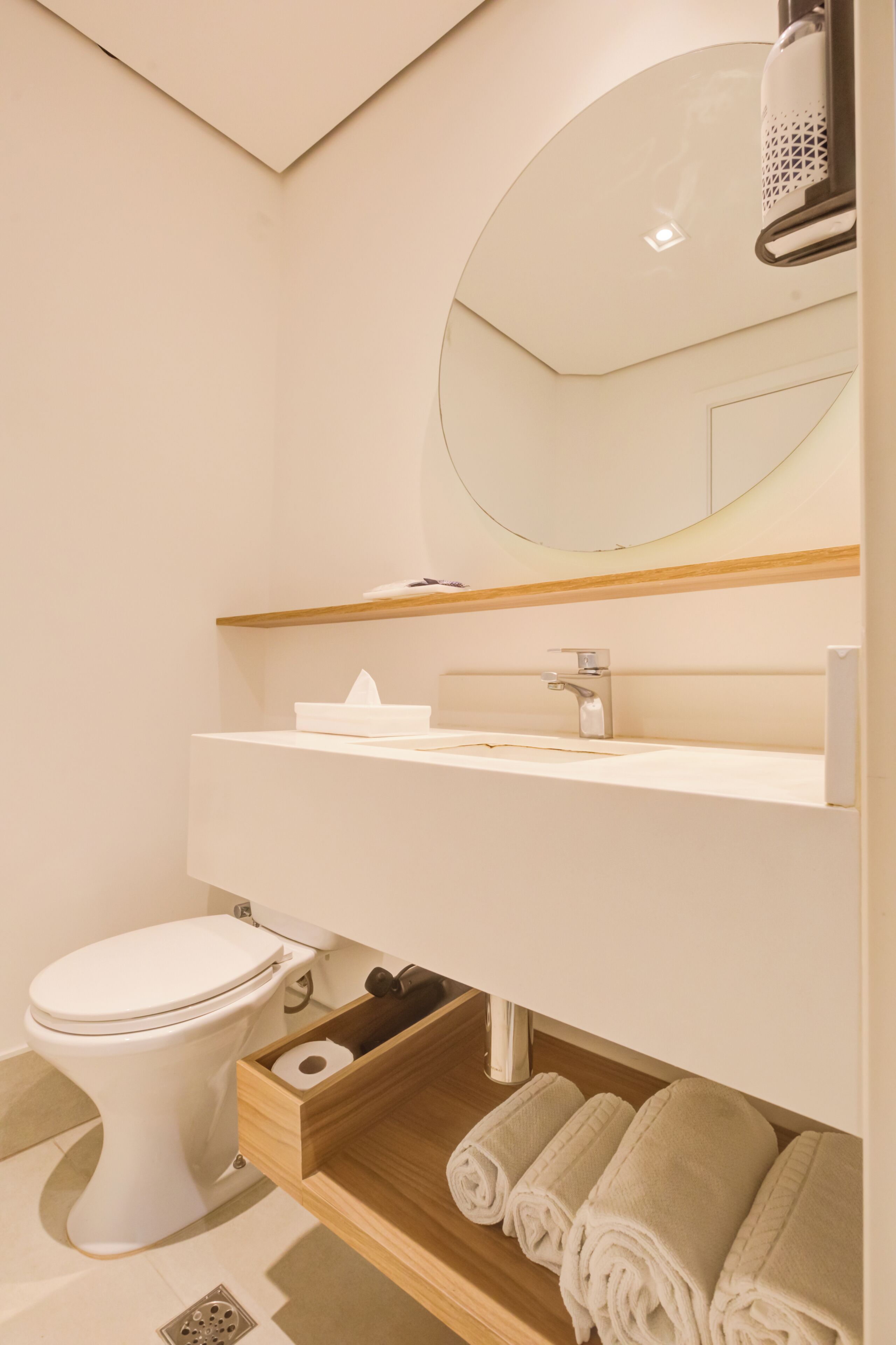 Une salle de bain moderne avec des toilettes blanches, un lavabo surmonté d’un miroir et un porte-serviettes avec des serviettes.