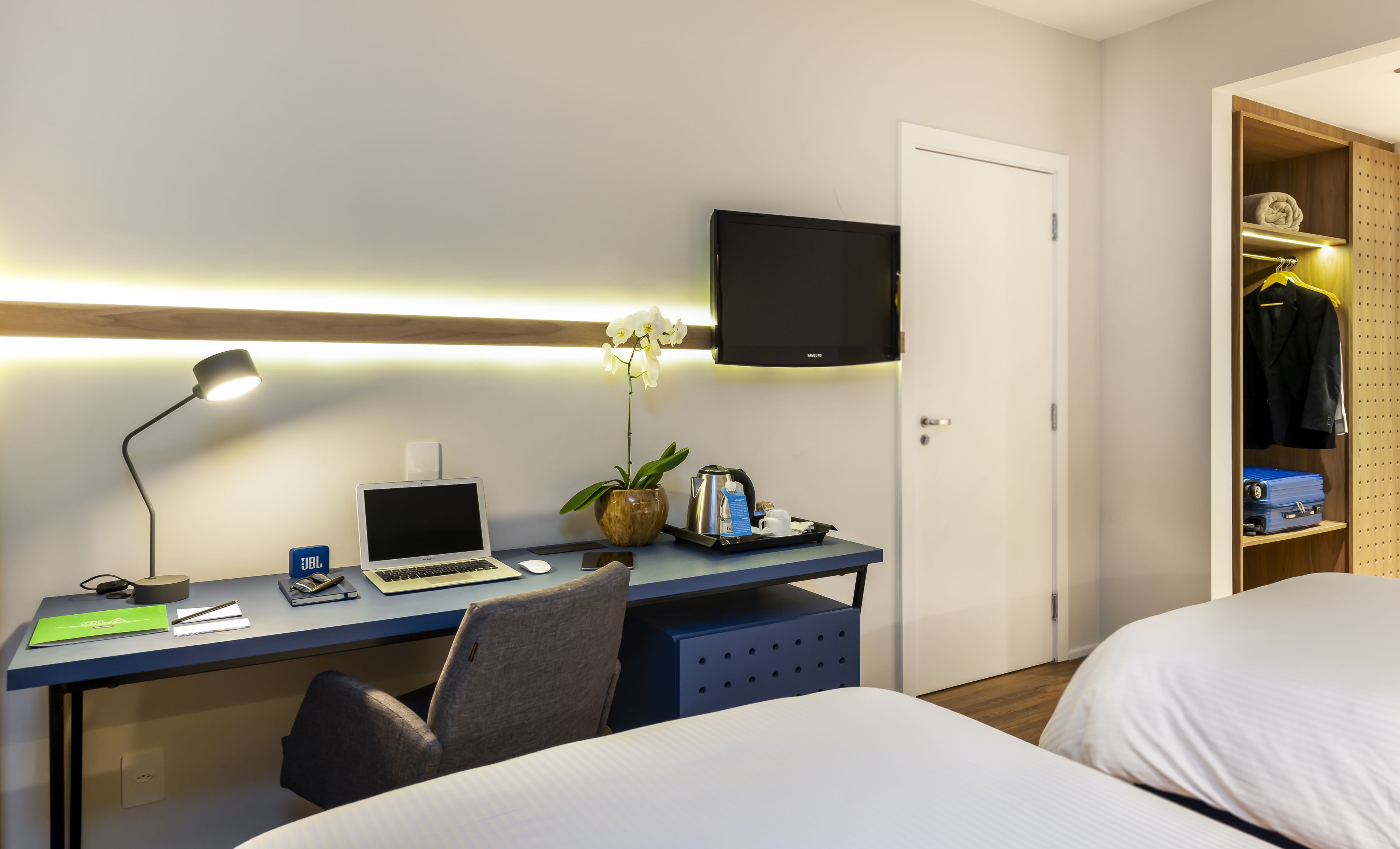 A hotel room with a desk, laptop, chair, bed, TV, and a wardrobe.