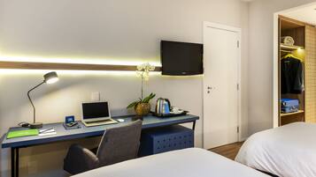 A hotel room with a desk, laptop, chair, bed, TV, and a wardrobe.