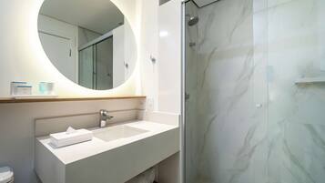 Une salle de bain moderne avec un miroir rond, un lavabo blanc et une douche à parois de verre.