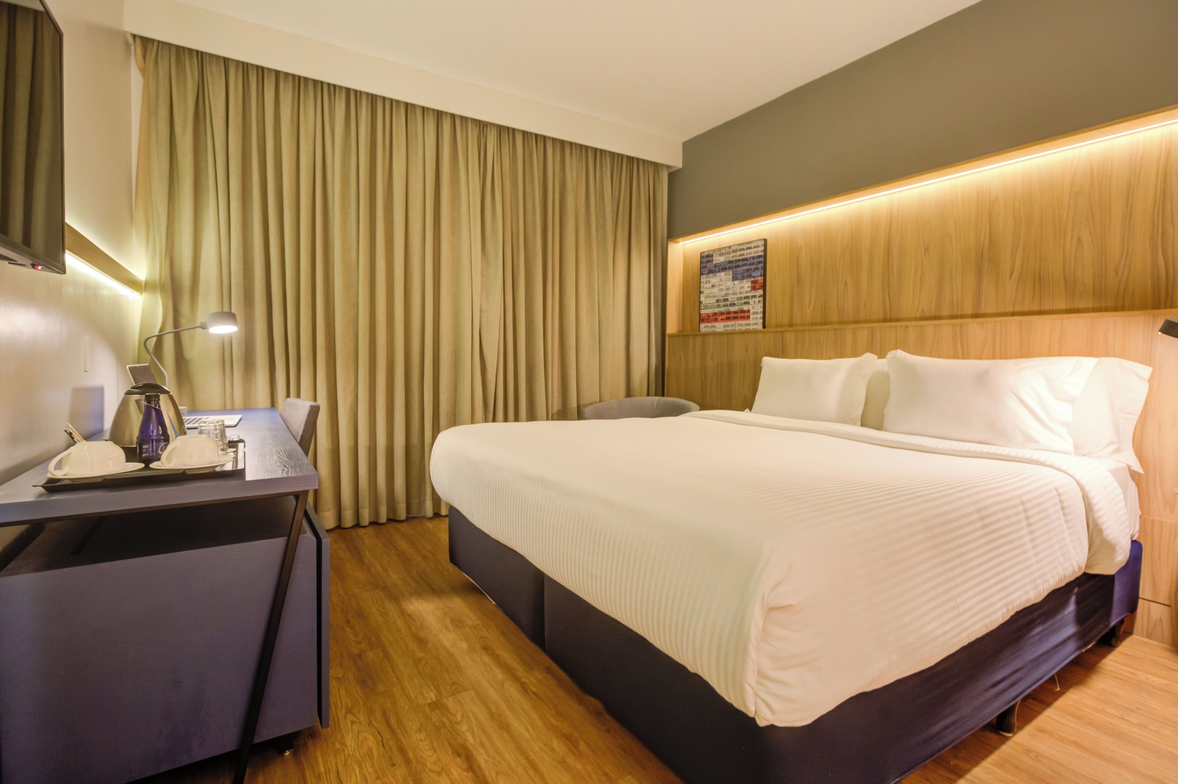Une chambre d’hôtel avec un lit, un bureau avec une lampe, une chaise et une tête de lit en bois.
