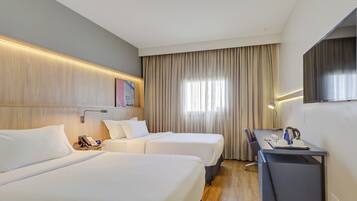 Quarto de hotel com duas camas, uma escrivaninha, uma cadeira, telefone e televisão de tela plana.