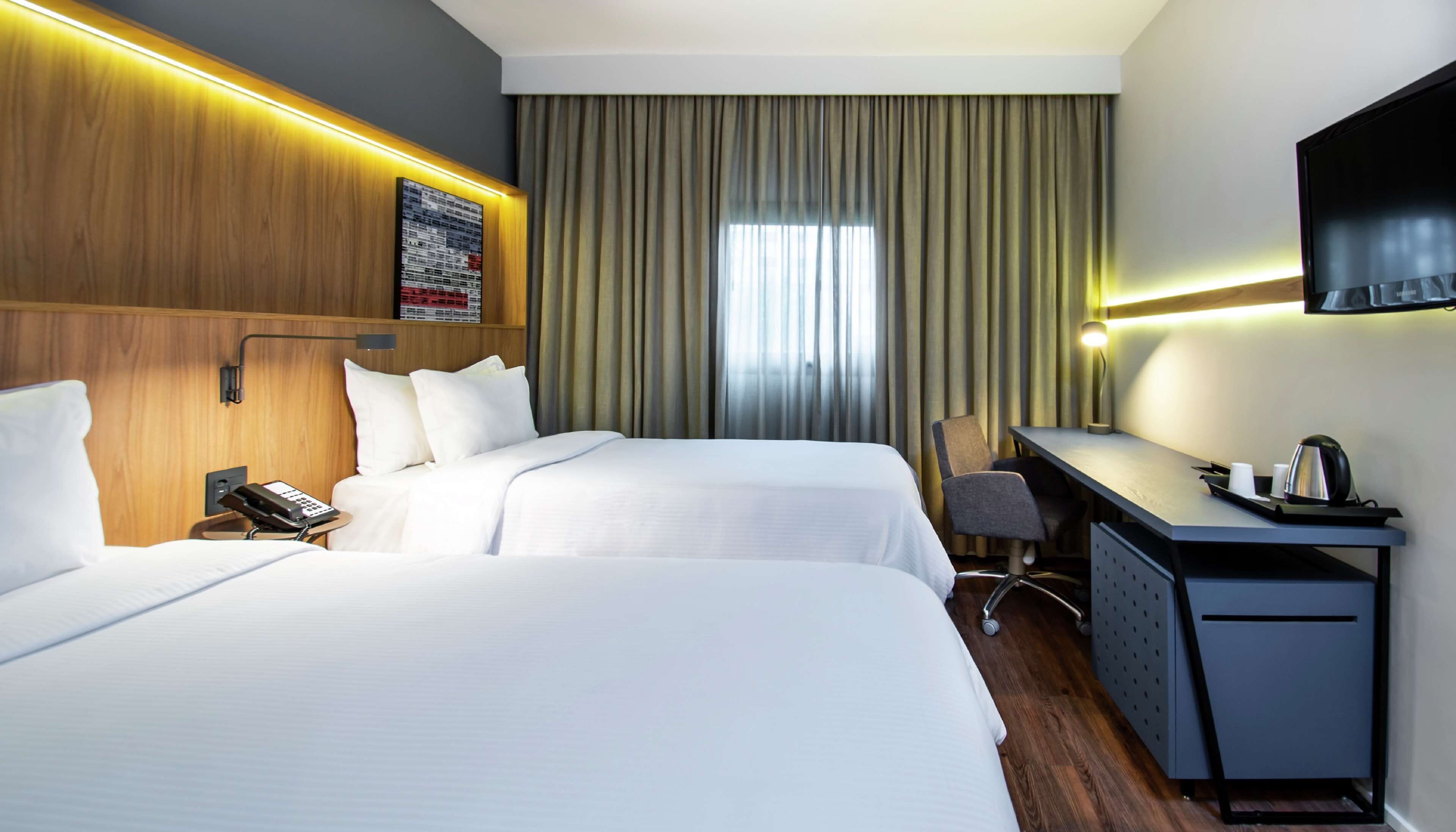 Habitación de hotel con dos camas, un escritorio, una silla, un televisor y una ventana con cortinas.