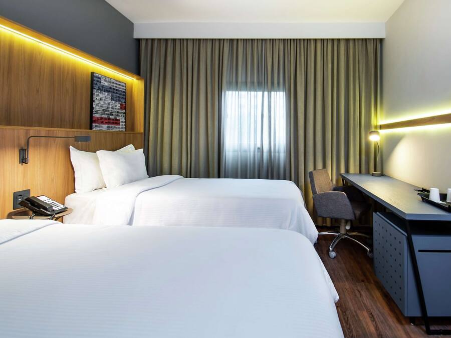 Habitación de hotel con dos camas, un escritorio, una silla, un televisor y una ventana con cortinas.