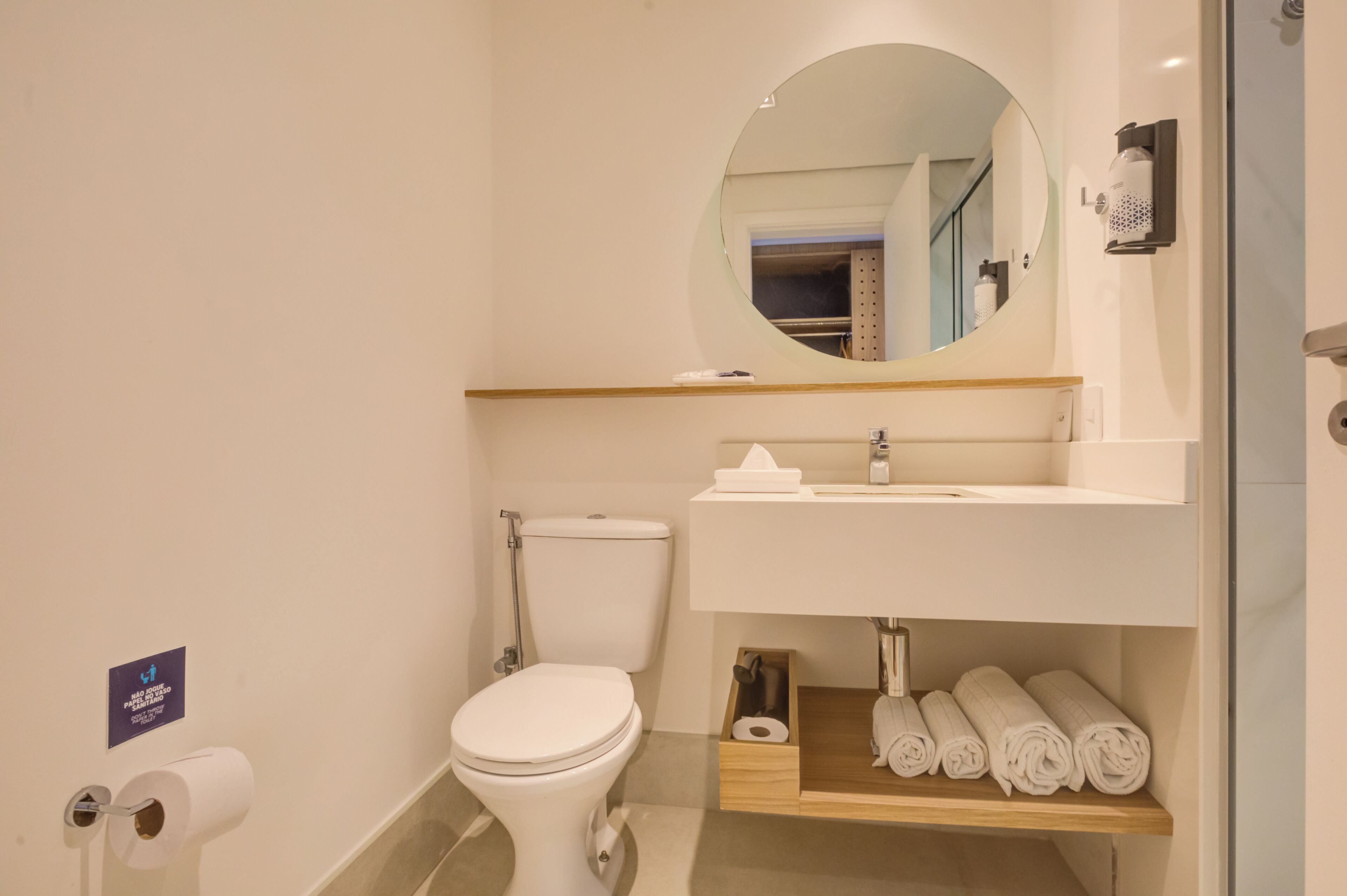 Une salle de bain moderne avec des toilettes, un lavabo et un miroir. On y trouve une étagère avec des serviettes et un porte-rouleau de papier toilette.