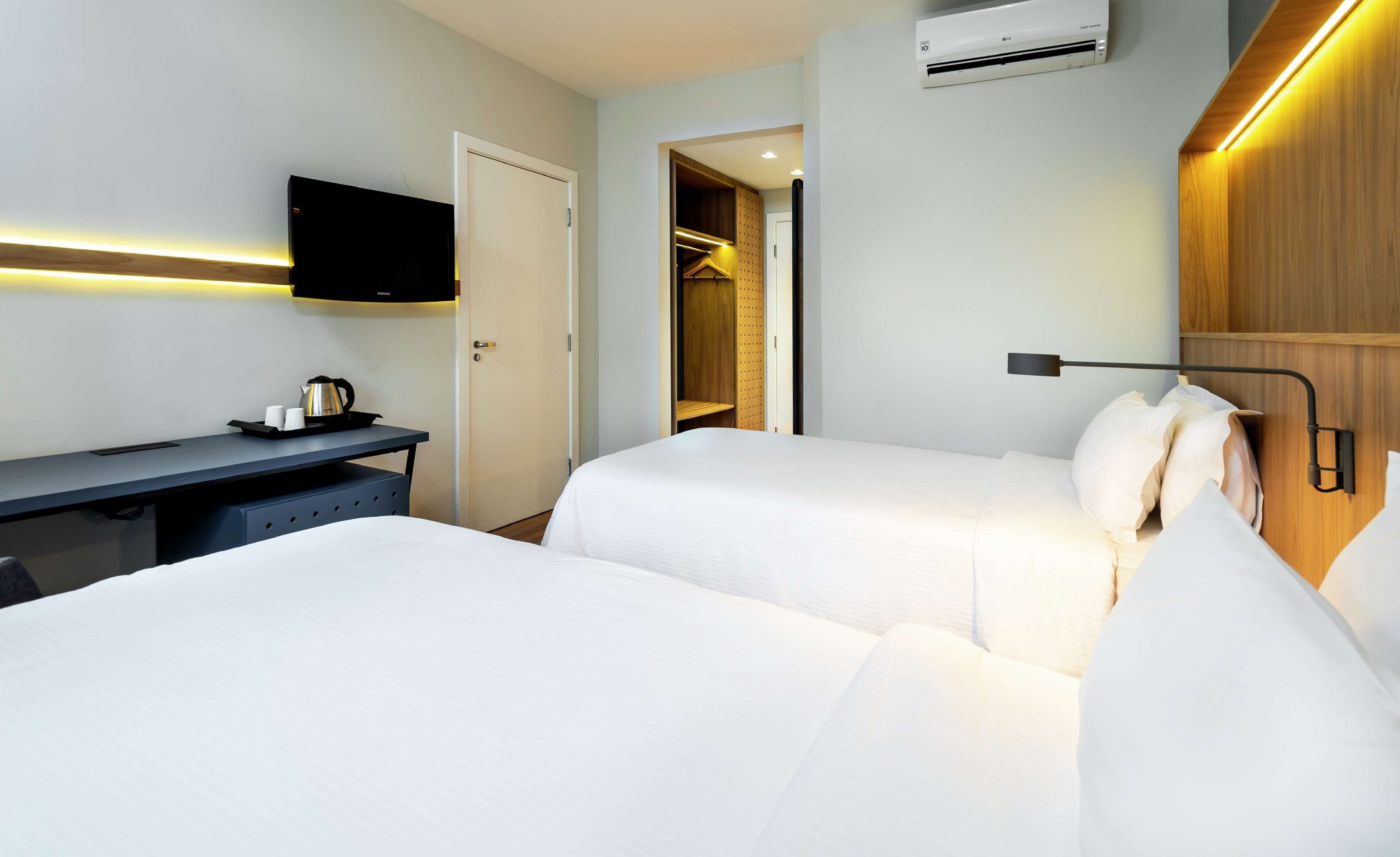 Quarto de hotel com duas camas, uma escrivaninha, televisão e guarda-roupa.