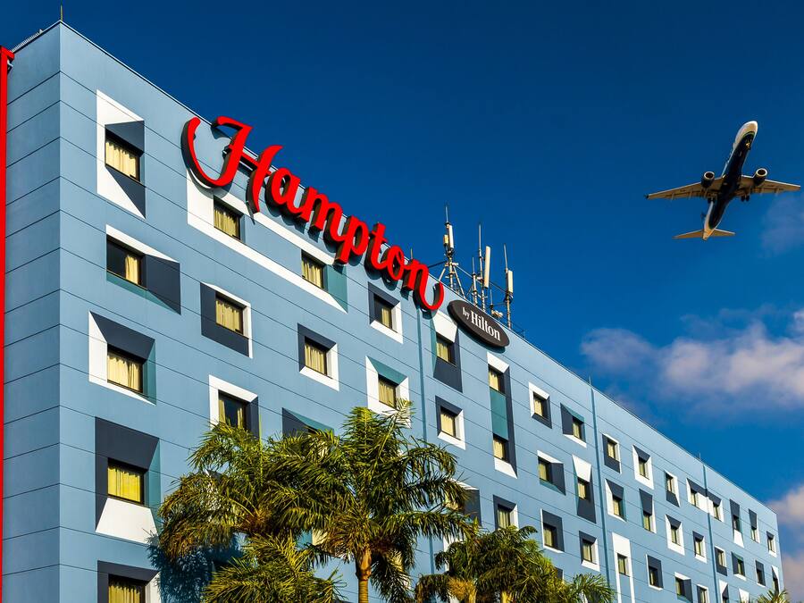 Hotel Hampton by Hilton con un cielo azul despejado y un avión en el fondo.