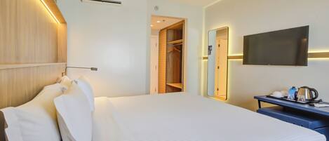A hotel room with a bed, a wardrobe, a desk with a kettle, and a flat-screen TV.