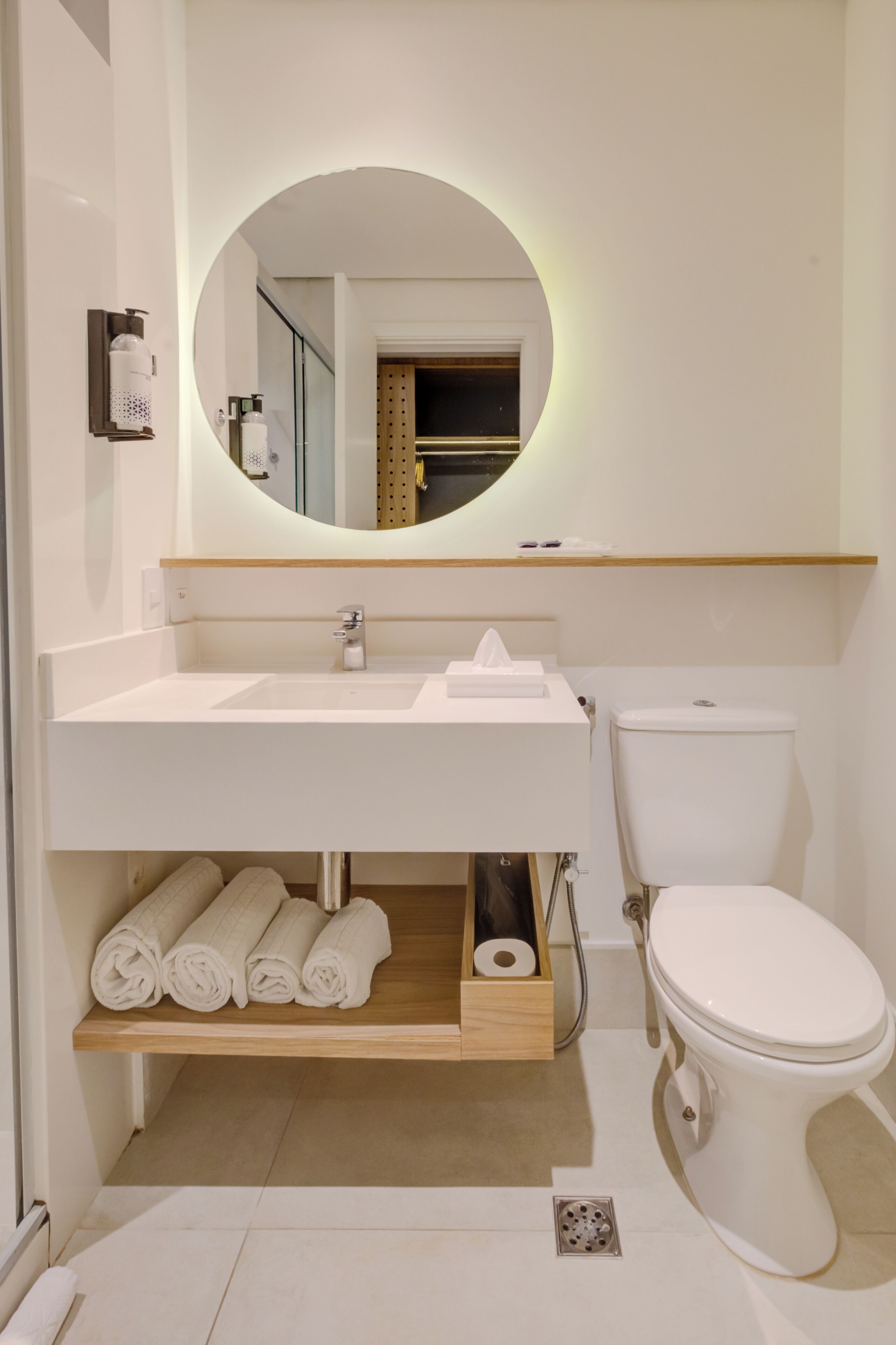 Un baño moderno con un lavamanos blanco, un inodoro y un espejo con marco circular.