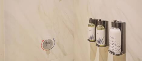 A bathroom with a marble wall, a showerhead, and three dispensers.