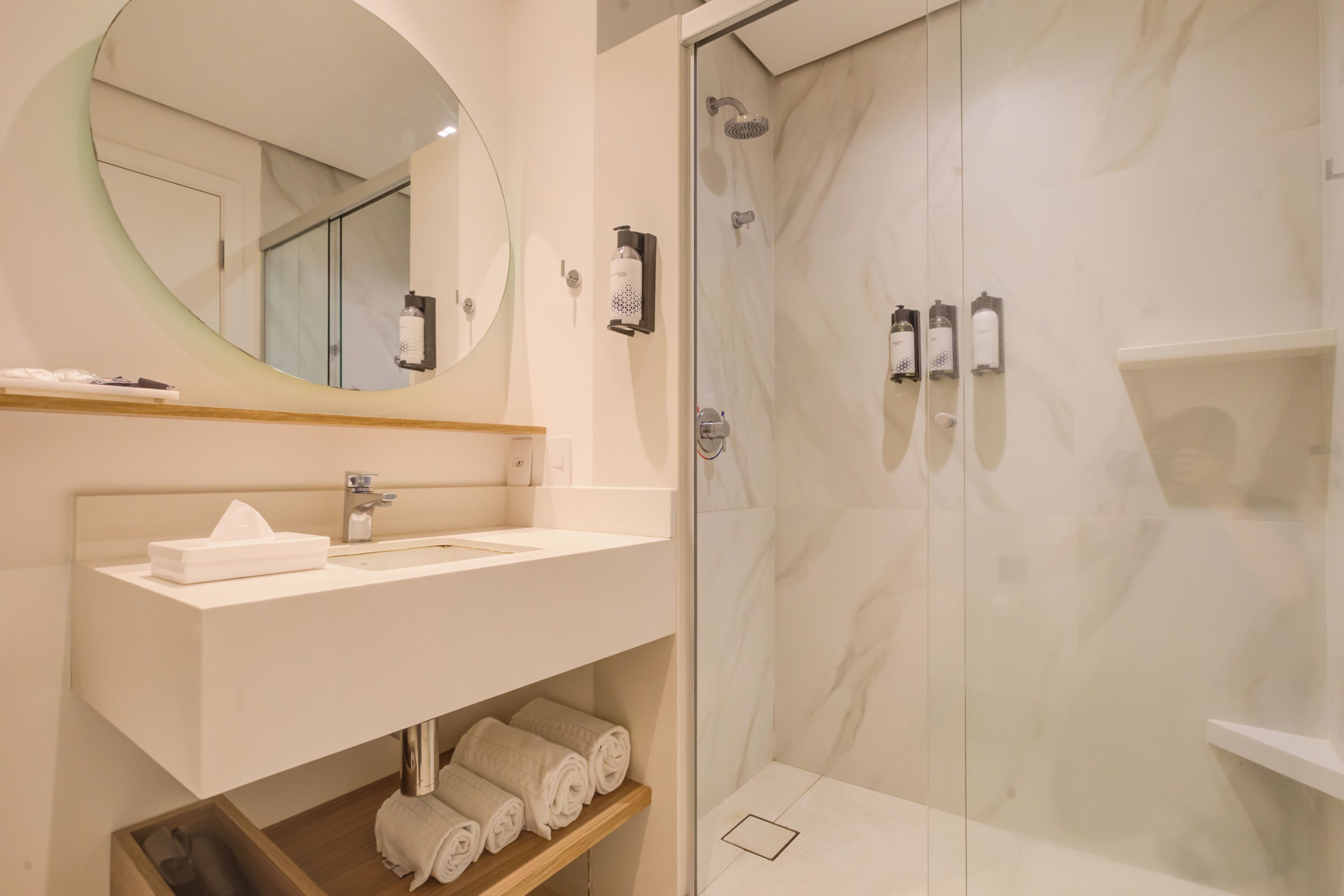 A modern bathroom with a white sink, mirror, and glass-enclosed shower.