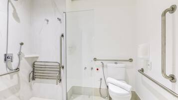 A modern bathroom with a glass shower enclosure, a white toilet, and a handrail.