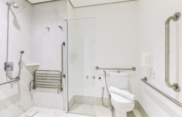 A modern bathroom with a glass shower enclosure, a white toilet, and a handrail.