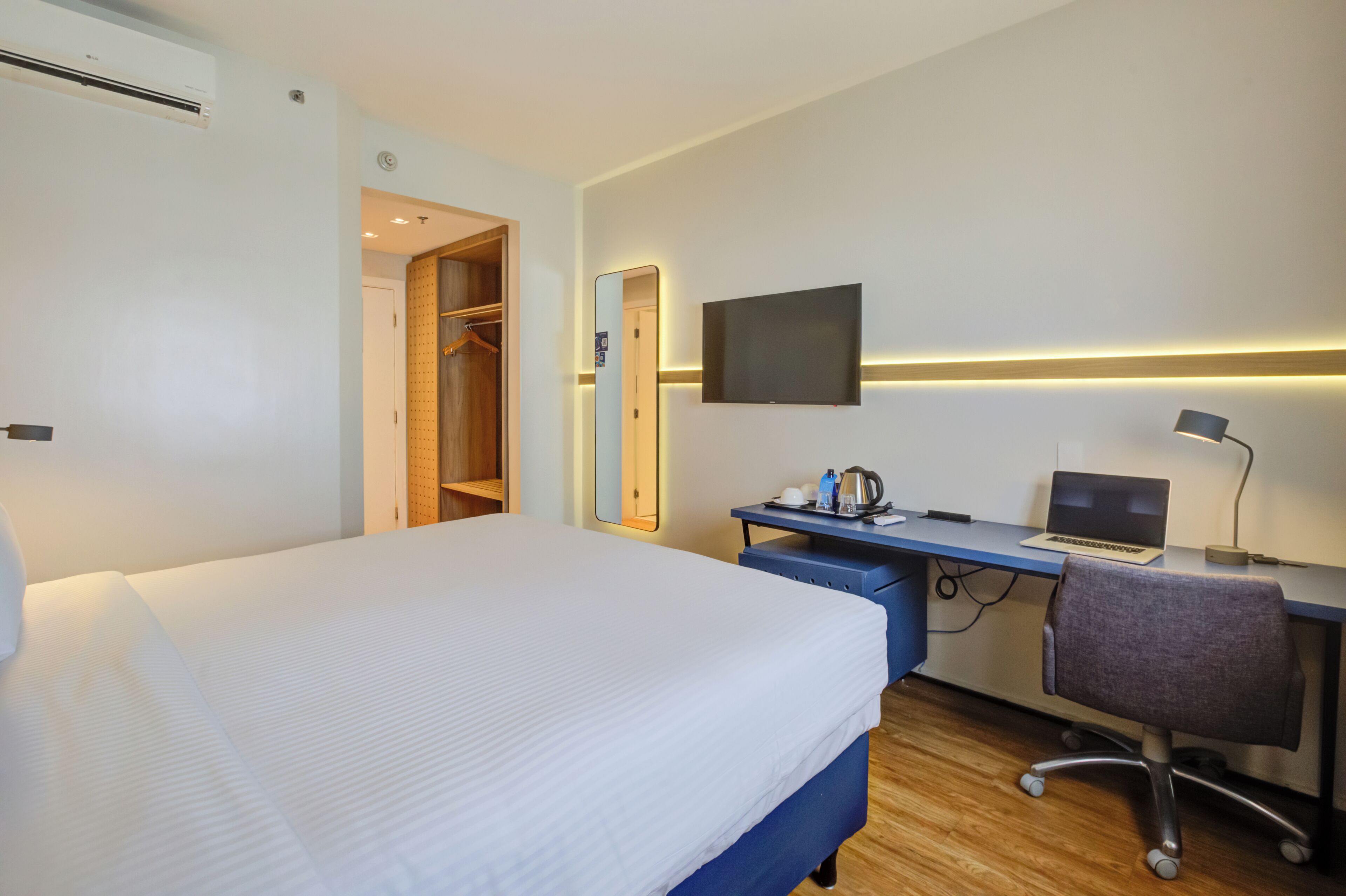 Une chambre d’hôtel avec un lit, un bureau avec un ordinateur portable, une télévision et un miroir.