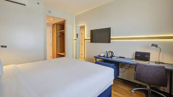 Une chambre d’hôtel avec un lit, un bureau avec un ordinateur portable, une télévision et un miroir.