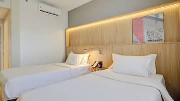 Habitación de hotel con dos camas individuales, cabecera de madera, aire acondicionado de pared y una mesita con teléfono.