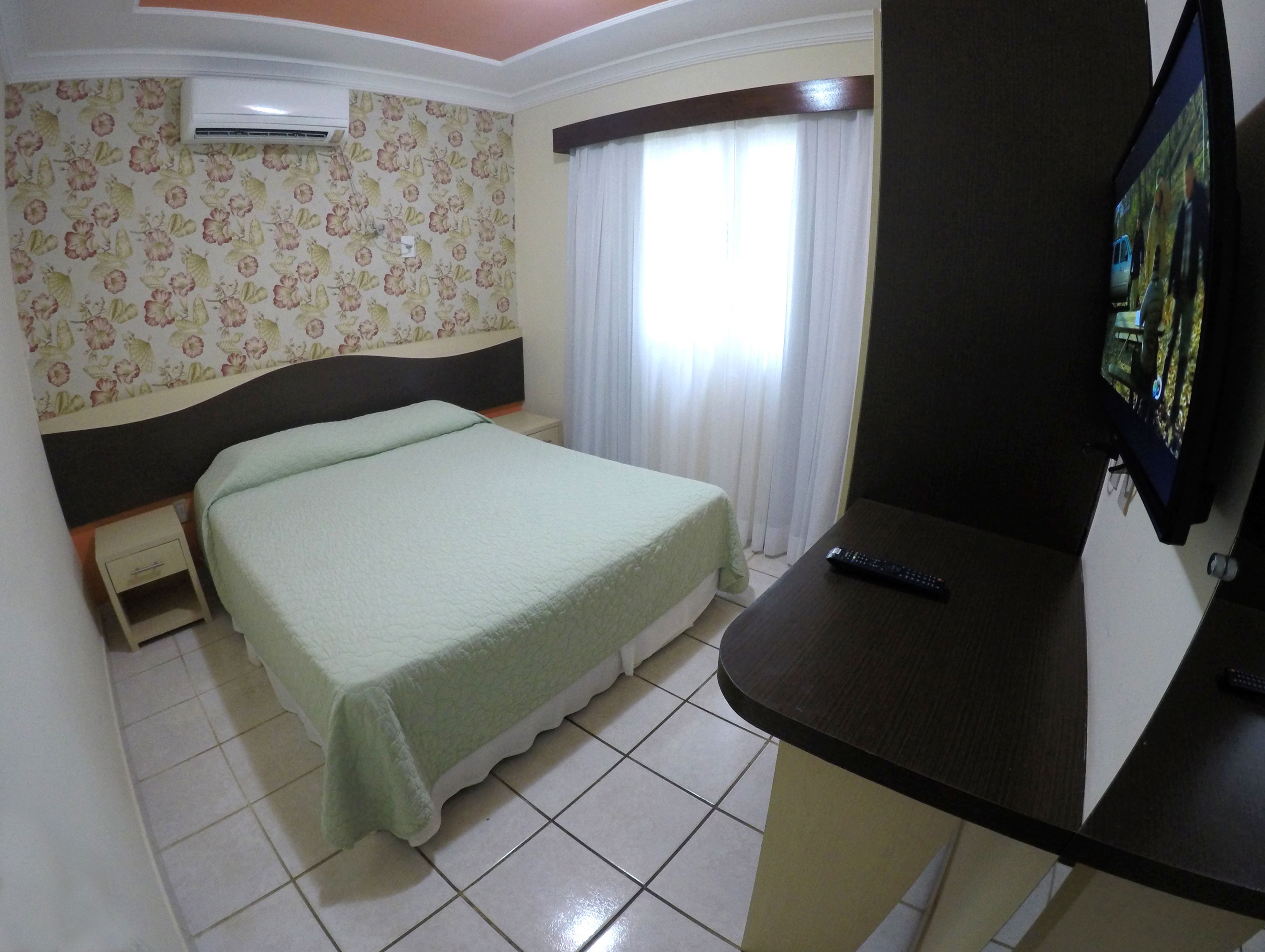 A hotel room with a bed, a nightstand, a TV, and a window with curtains.