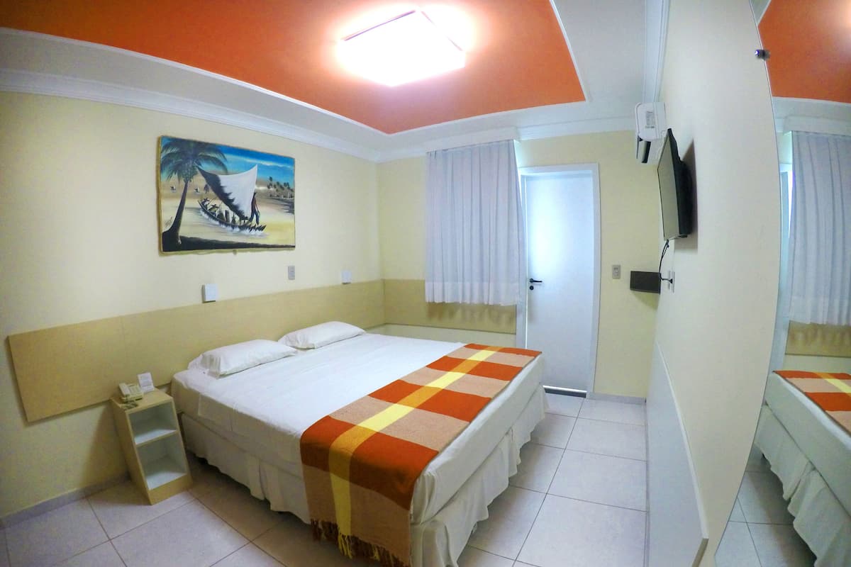 A hotel room with a bed, a nightstand, a painting, a television, and a door.