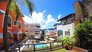 Ein Innenhof mit Swimmingpool, Palmen und einer Holzbank.
