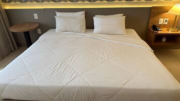 A neatly made bed with a quilted white duvet, a wooden bedside table with a lamp, and a wall with a geometric patterned design.