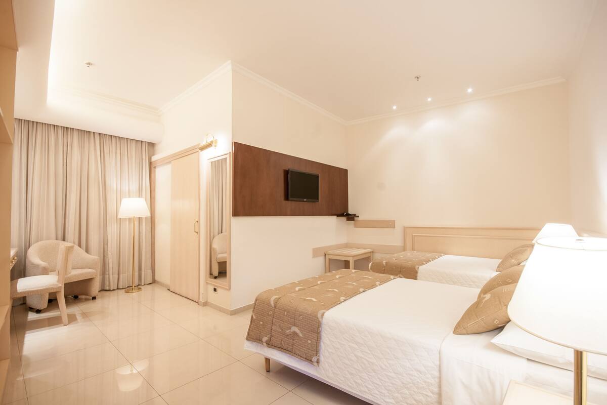 A hotel room with a bed, a chair, a desk, a TV, and a mirror.