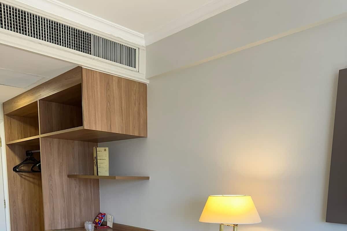 A modern hotel room with a wooden desk, a lamp, a mini fridge, and a trash bin.