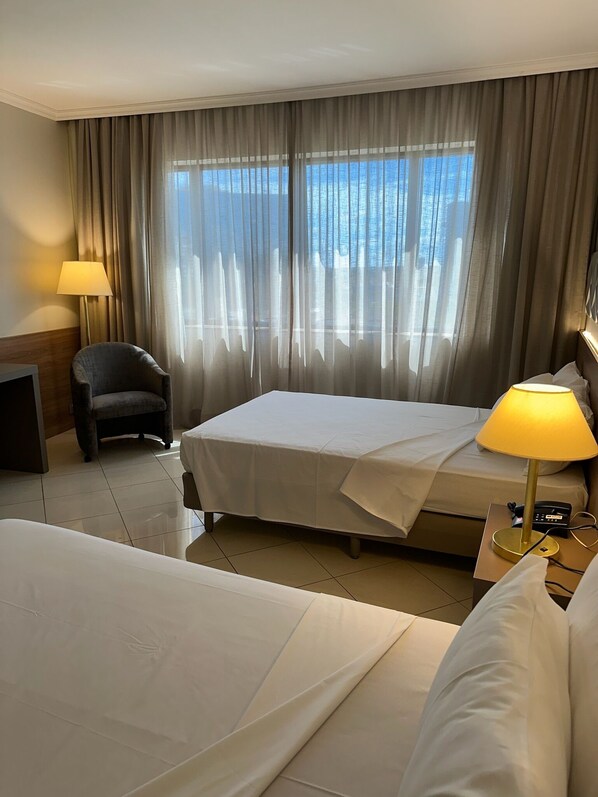 A hotel room with a bed, a chair, a desk, a lamp, and a window with curtains.
