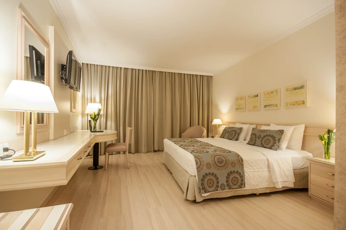 A hotel room with a bed, bedside tables, a desk, a chair, a TV, and curtains.