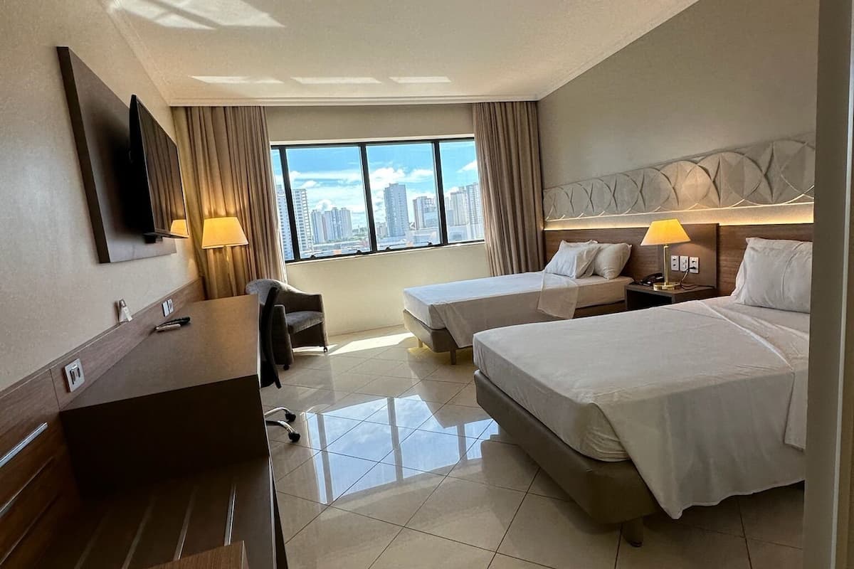 A hotel room with two beds, a desk, a chair, a TV, and a city view.