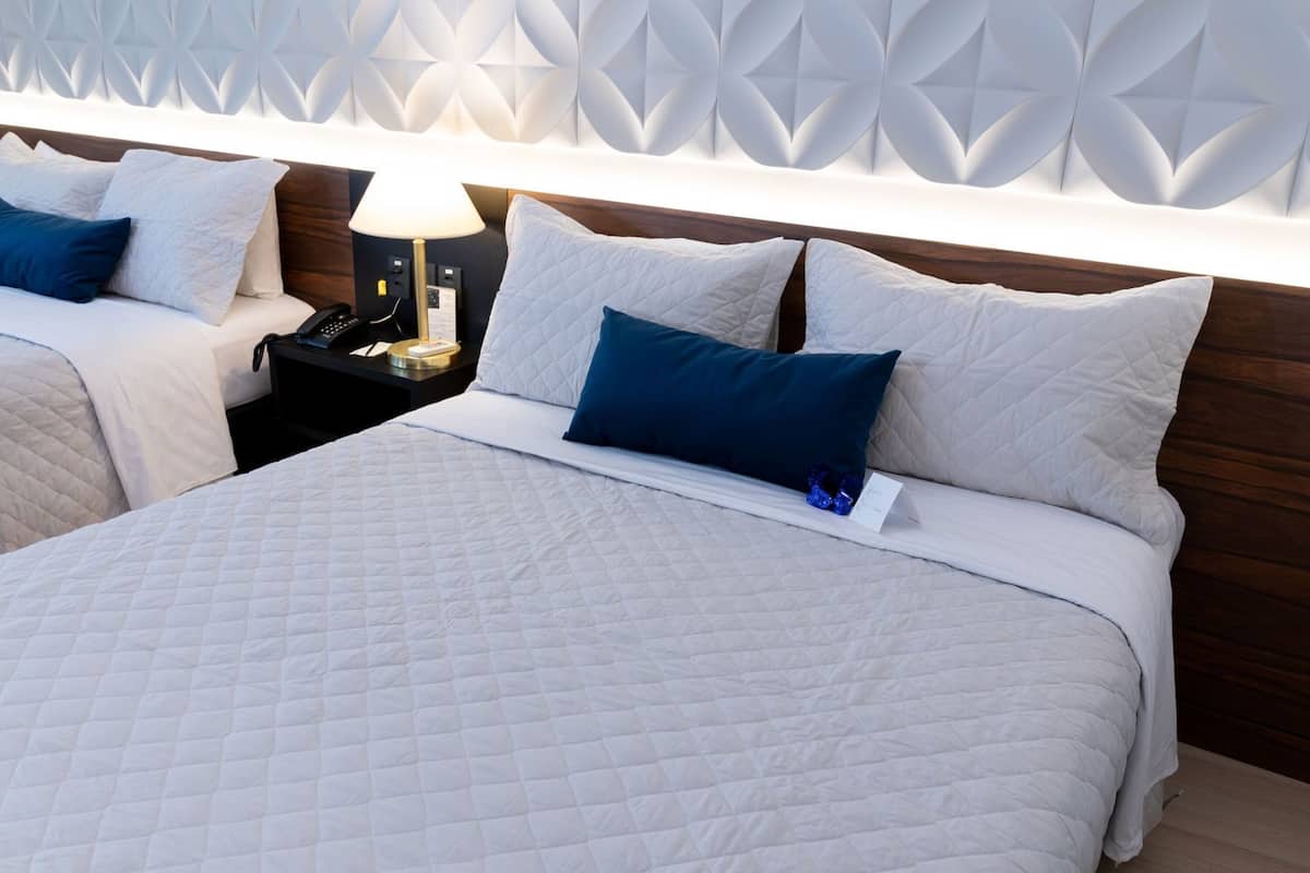 A hotel room with two beds, a nightstand with a lamp, and a decorative wall panel.