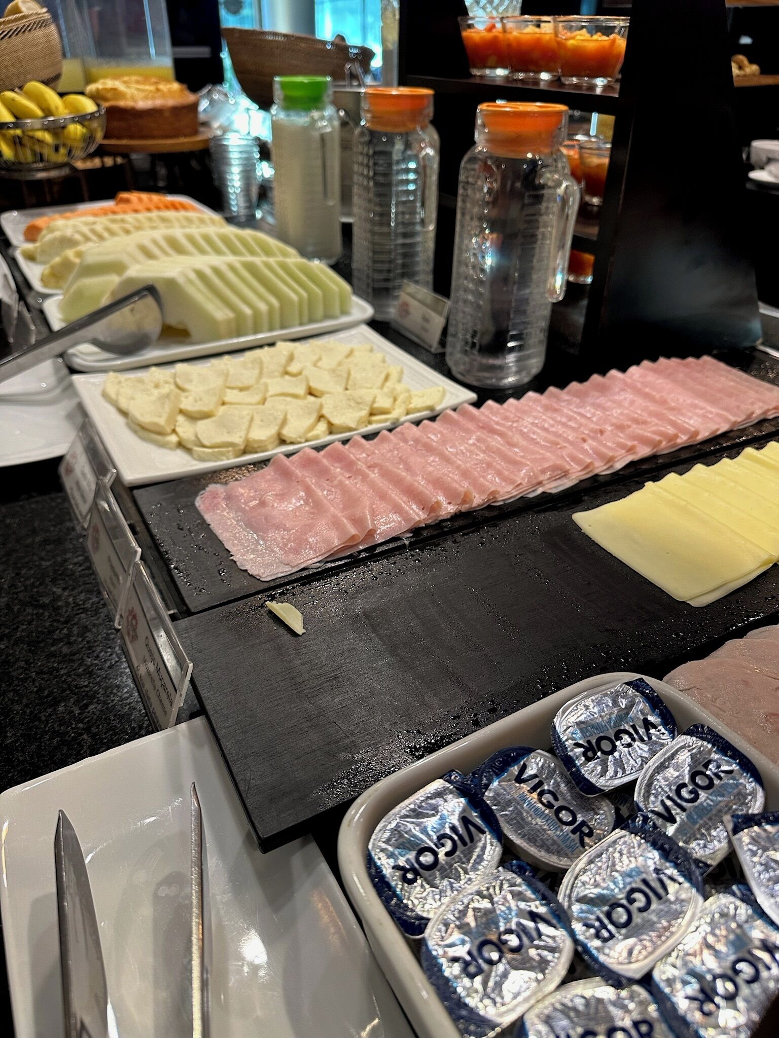 Buffet com diversos alimentos, incluindo carnes fatiadas, queijos e acompanhamentos.