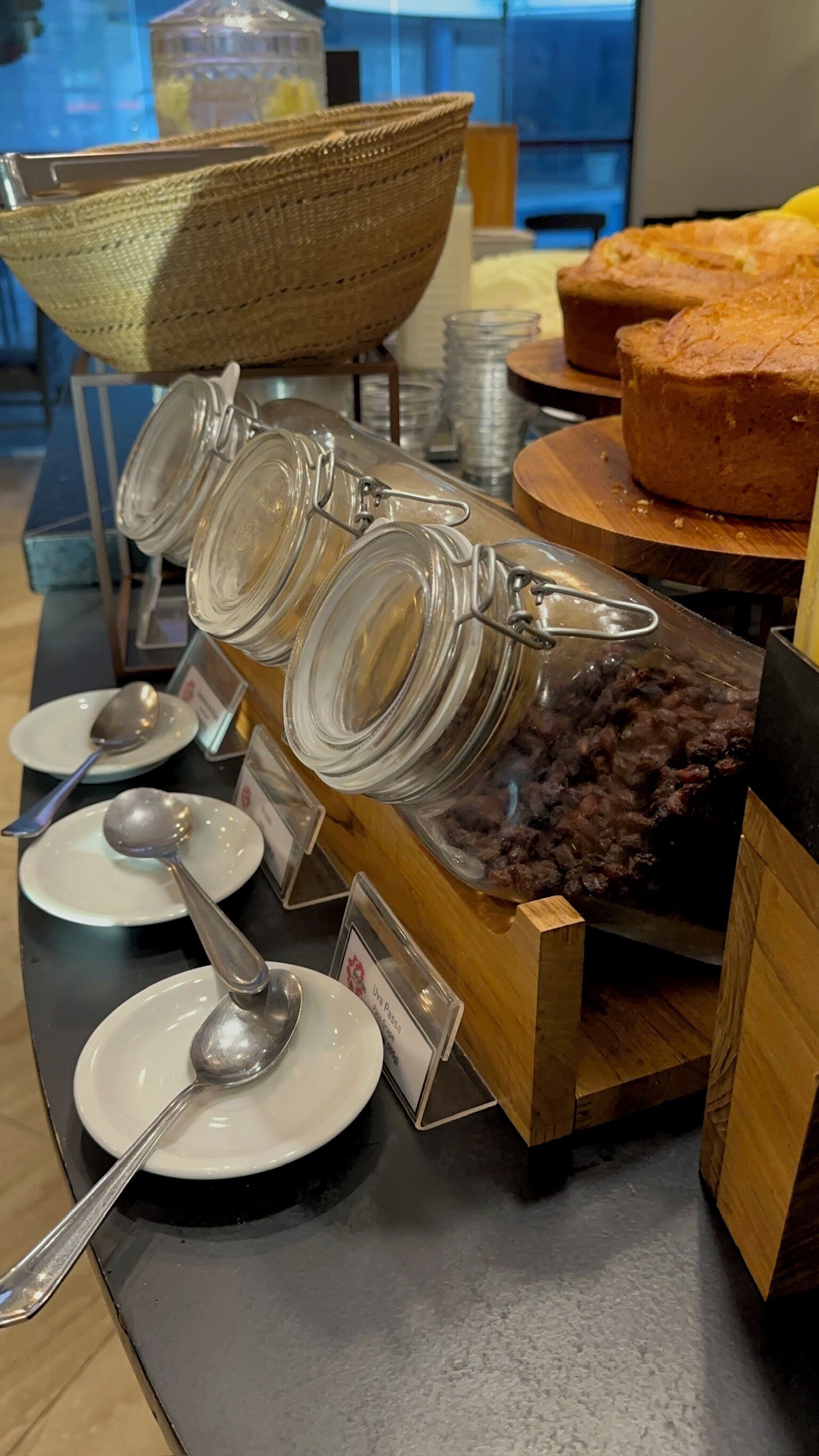 A buffet setup with clear glass containers holding various food items, accompanied by serving spoons and plates.