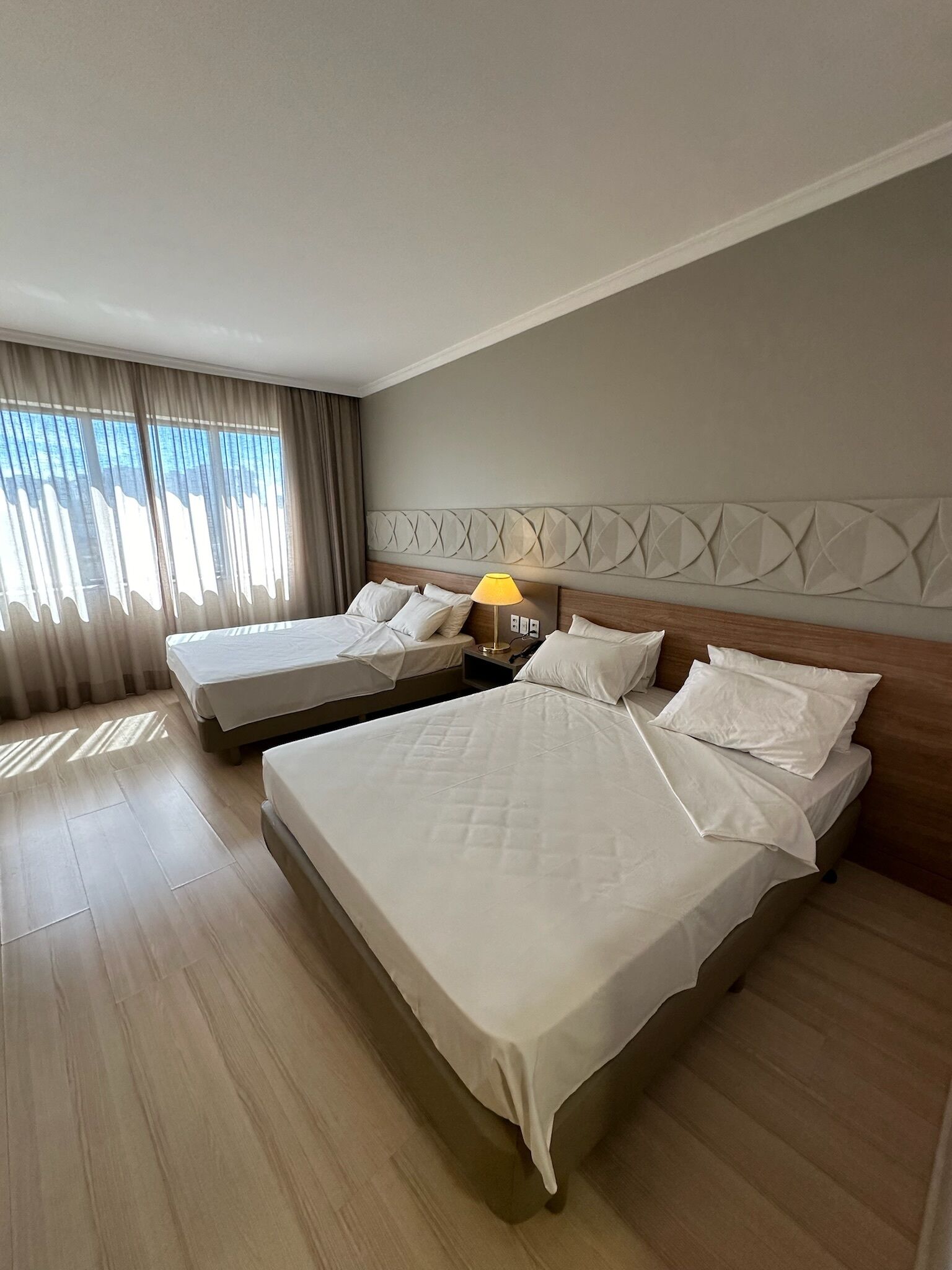 A hotel room with two beds, a nightstand with a lamp, and a decorative headboard.
