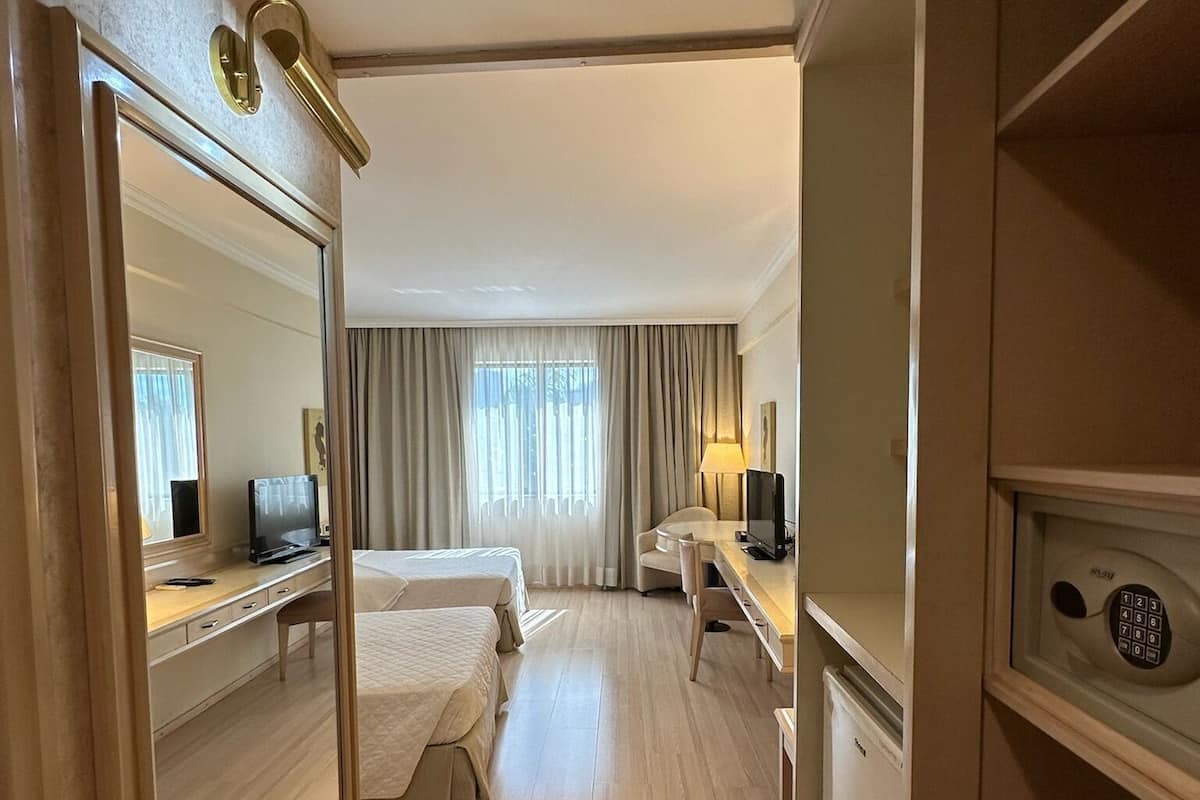 A hotel room with a bed, a desk, a chair, a TV, and a safe.
